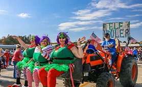 Three women dressed as elves wave from the back of a red tractor.