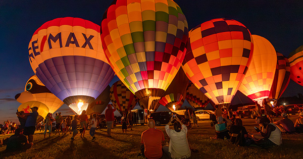 Children watch as brightly colored balloons lift off against the night sky.