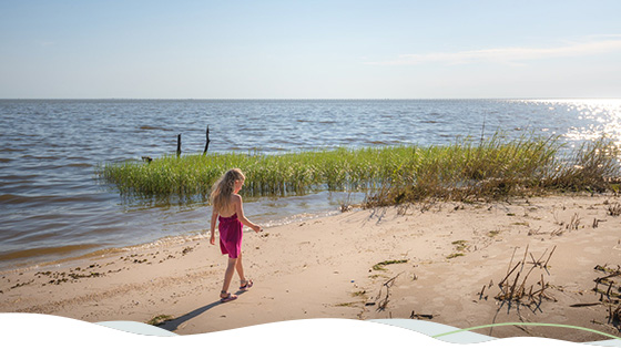 A girl in a pink dress walks along a beach in Louisiana.