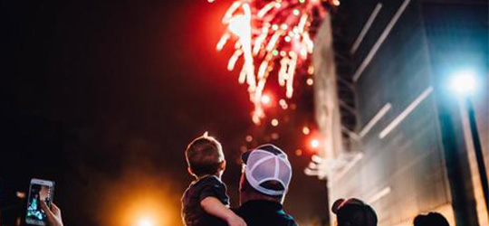 A father holds his child during a dazzling fireworks show.