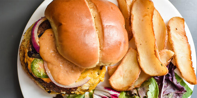 A juicy burger covered in remoulade sauce, served with French fries.