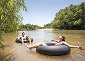 Two people float in black inner tubes on a muddy Louisiana river.