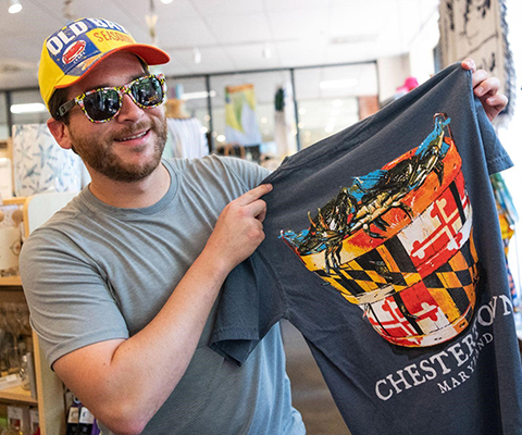 Picture of of a man wearing an Old Spice ball cap and holding up a Maryland Pride T-Shirt.