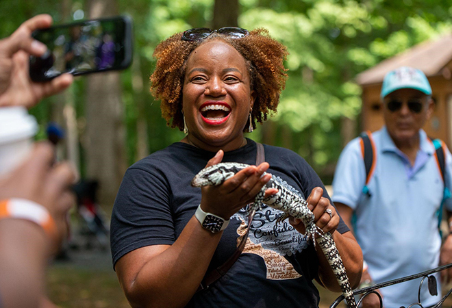 Picture of a woman holding a lizard and laughing for a photographer during a Juneteenth Celebration.
