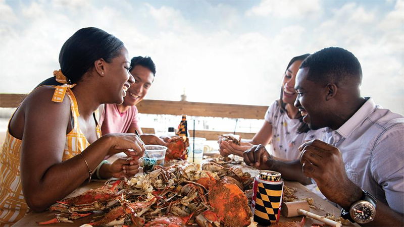 Picture of two couples enjoying eating Maryland Steamed Crabs outside on a deck.