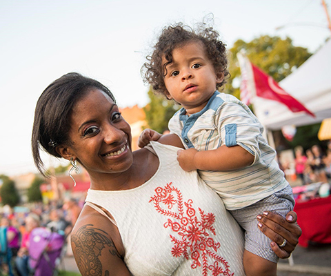 A picture of a mother carrying her child on her side at a festival.