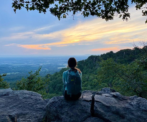 Picture of a girl sitting on the mountain rocks overlooking the scenic view.