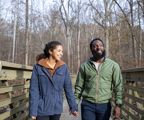 Picture of a happy couple holding hands while taking a walk across a wooden bridge.