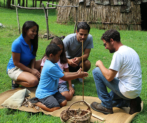 Picture of three adults teaching two children hot to start a fire with a stick.