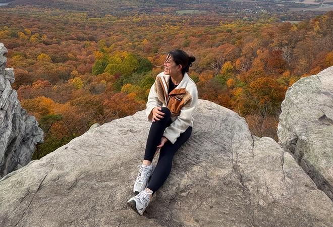 Picture of a woman sitting on top of a rock in the mountains and enjoying the beautiful surrounding Fall Foliage.