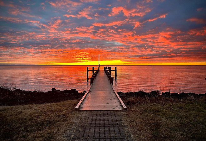 Pier leading into sunset over the water.