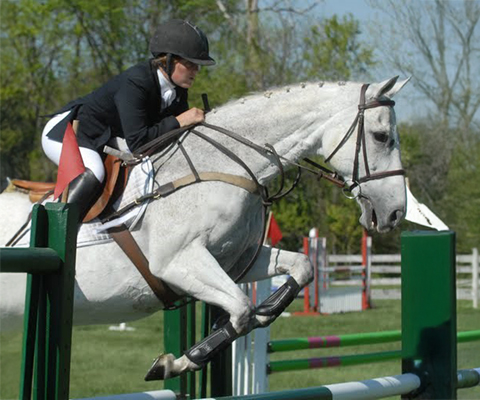 Rider on a white horse jumping over a fence.