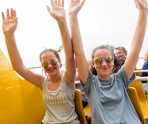 Two girls smiling with their arms up on an amusement ride.