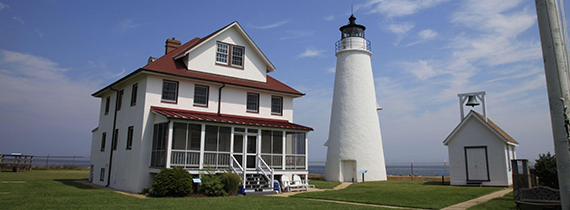 A white lighthouse and white house with a red roof next to it.