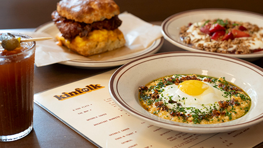 A table of brunch favorites, including a breakfast sandwich, yogurt with granola and berries and sunnyside up eggs, as well as a water in a glass that says