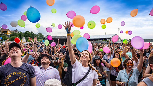 A crowd of concert-goers at RiverBeat Music Fest in Memphis reaches up toward a colorful balloon drop