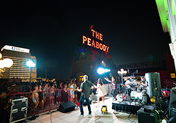 A band playing in front of a crown at a Peabody Rooftop Party. 