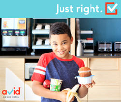 A picture of a child at holding an apple, a banana, cereal and a muffin from the continental breakfast area at Avid Hotel. The words 