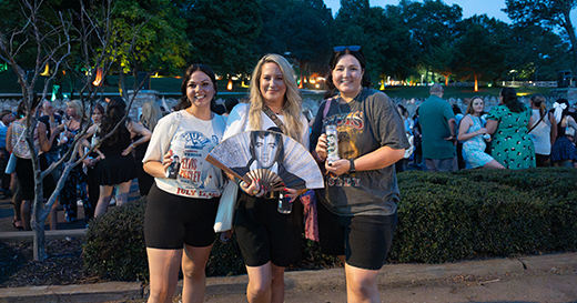 Elvis fans posing with souvenirs at Elvis Week with a crowd in the background.