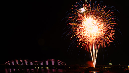 Fireworks over the Mississippi River in downtown Memphis with the Hernando de Soto Bridge illuminated with Mighty Lights in the background.