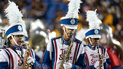 Three musicians in full marching band uniform play their instruments during a show.