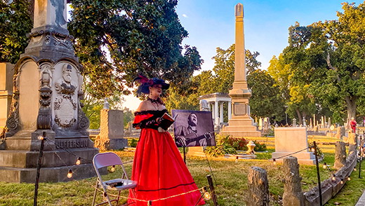  A woman dressed up for a living-history ghost tour at Elmwood Cemetery with tombstones in the background.