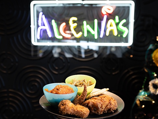 Plates of soul food in front of the neon Alcenia's sign at Alcenia's.
