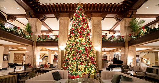 Large Christmas tree decorated in gold, green and red decor inside The Peabody lobby with garland on the banister. 