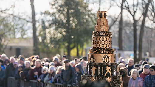 A crowd gathered around Elvis' birthday cake, which is decorated in gold and black icing with a crown on top.