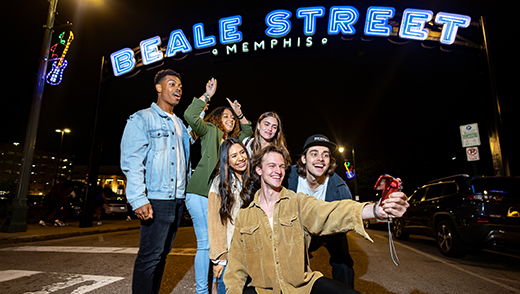 A group of friends posing for a selfie under the neon Beale Street Memphis sign on Beale.