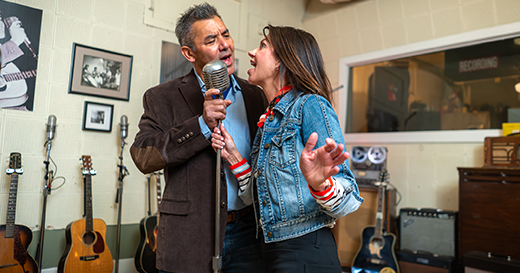 A couple singing together at a mic for a photo op inside Sun Studio.