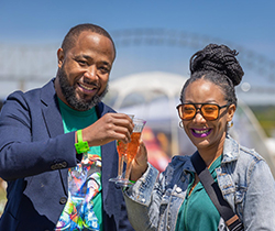 A couple toasting their glasses at Mimosa Festival Memphis with the Hernando De Soto Bridge in the background.