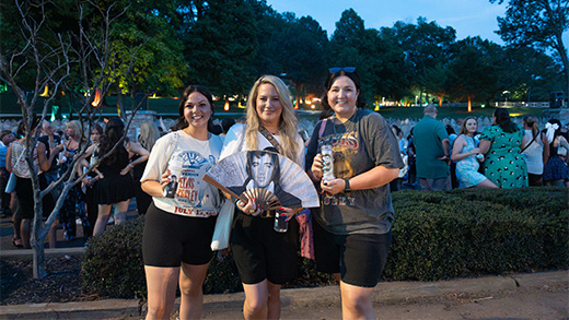 Three women smiling for a photo while holding Elvis memorabilia.