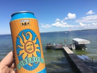 A man holding a can of Oberon Ale beside an inland lake. 