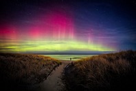 A person standing on the shore of Lake Superior under the northern lights.