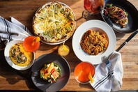 A spread of pizza, pasta and other meals with craft cocktails on a table. 