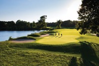 A group of golfers playing beside an inland lake. 