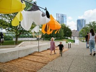 A family walking beside a public art installation of large lanterns shaped like gold fish.