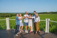 A group of friends holding glasses of whine on a balcony over a vineyard.
