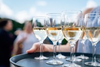 A woman carrying a tray of glasses of white wine. 