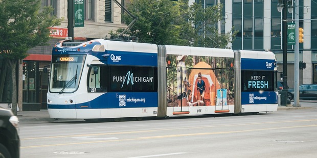 The QLINE tram wrapped with a camping image and the Pure Michigan logos.