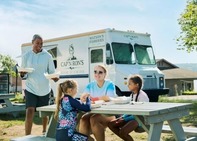 A family dining at a picnic table near a food truck on the coast of Lake Superior. 