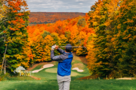 A man playing golf on a course surrounded by fall trees. 