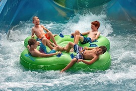 A family on a group raft coming out of a water slide. 