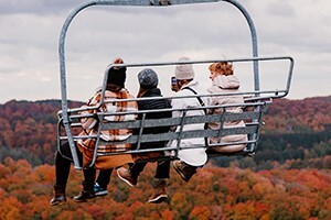 A group of women on a scenic chairlift ride over fall trees. 