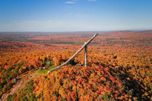 The artificial ski jump atop a hill covered with fall trees. 