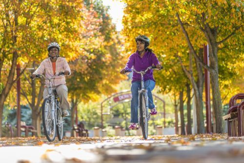 Two woman riding bikes on a paved path in Petoskey during fall. 
