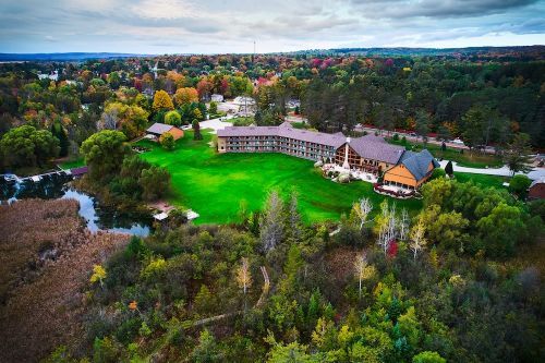 A lodge surrounded by fall forests and a lush lawn. 