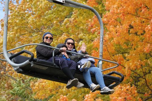 A man, woman, and child on a chairlift traveling past fall trees. 