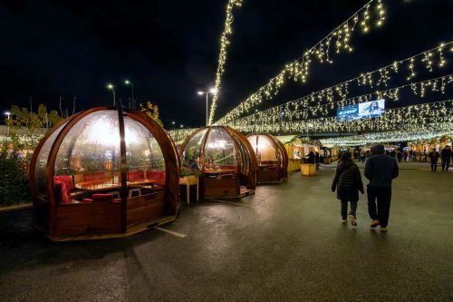 People walking in an outdoor Christmas Market at night beside dining igloo tents. 